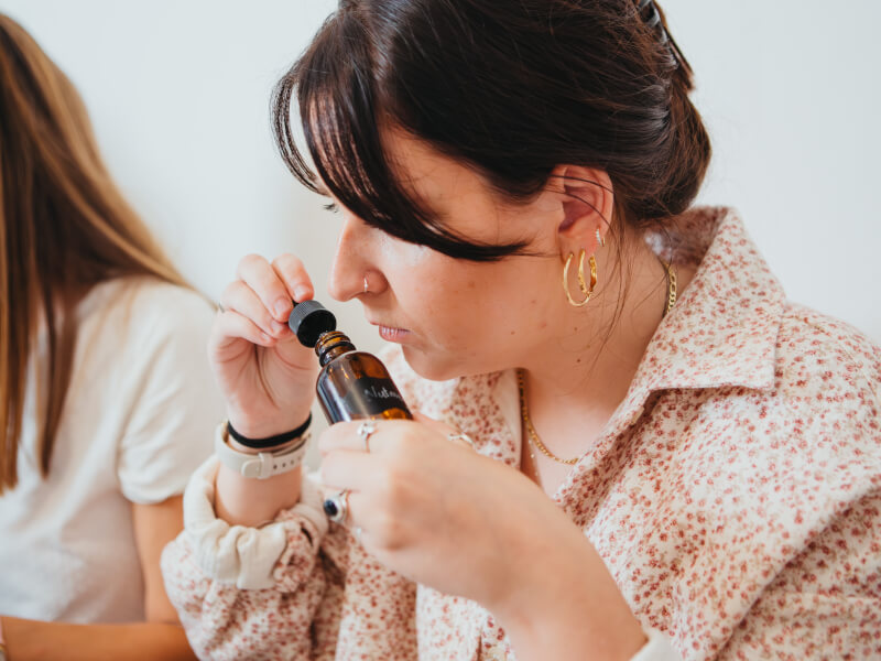 A woman at a perfume making class smelling a small amber bottle with a dropper